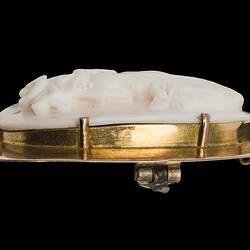 Profile of oval white cameo of female bust facing left. She wears a draped garment and has ribbons in her hair. Plain gold setting.