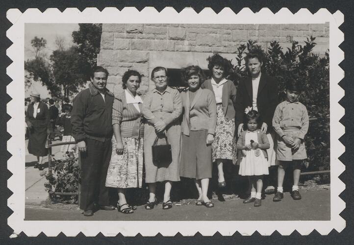 Group of six pose with two young children in front of a stone brick wall and trees.