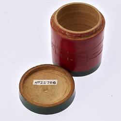 Open red painted, cylindrical wooden box. Dark green trim around lid and base.