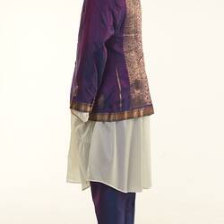 Purple sari two-piece suit and matching tie, long off-white shirt. Gold detail on jacket edging. Left profile.