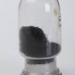 Domed cylindrical jar containing black stringy botanical sample.
