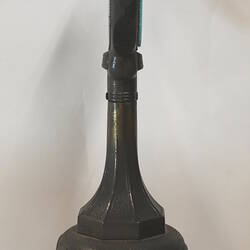 Clock with clear glass face on dark green painted stand, side view.