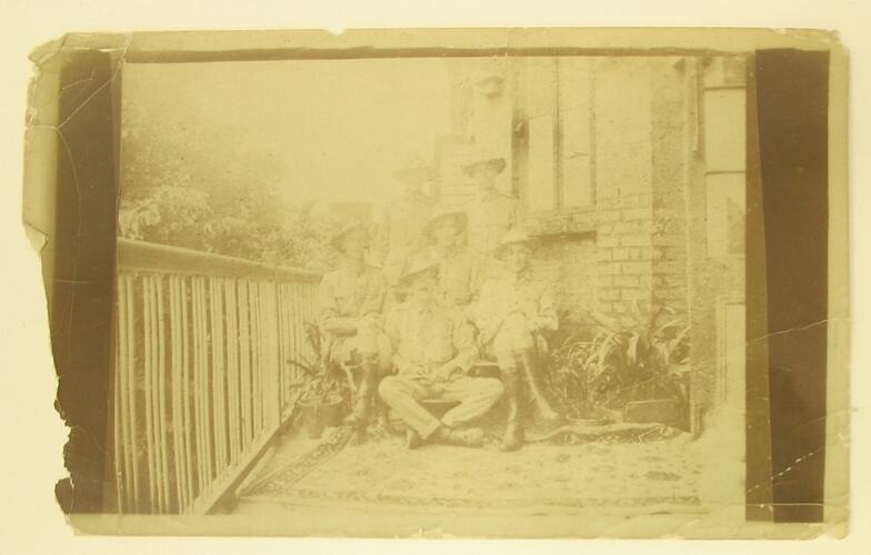 Six men in military uniform posed seated on balcony.