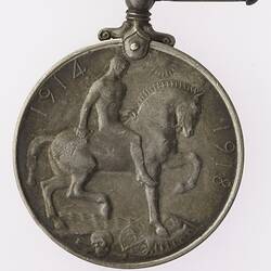 Round silver coloured medal with man on horseback and text surrounding.