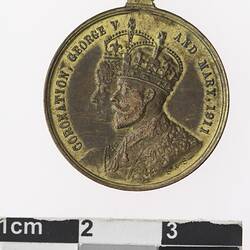 Round gold coloured medal with profile of a man and woman with crowns, text surrounding.