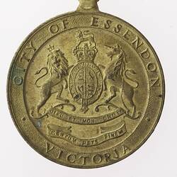 Gold coloured medal with coat of arms, reading "CITY OF ESSENDON VICTORIA."
