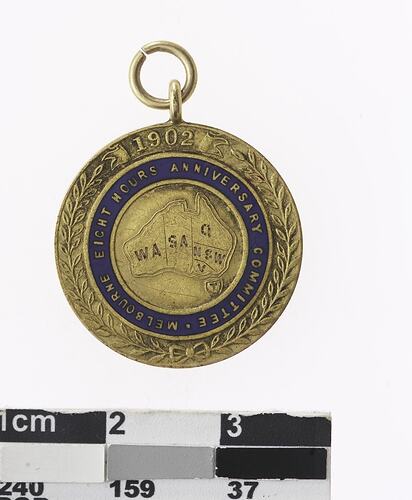 Round gold coloured medal blue enamel ring with text, leaf pattern around edge.