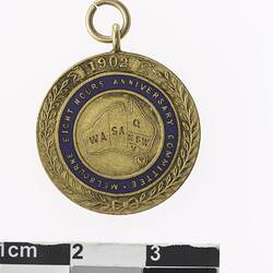 Round gold coloured medal blue enamel ring with text, leaf pattern around edge.