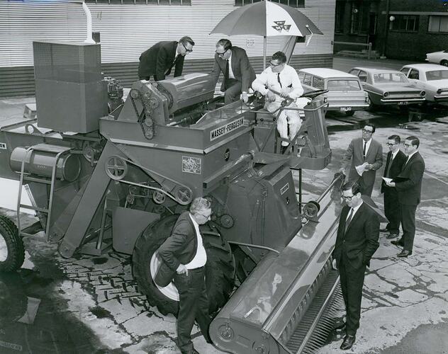 Group of men examining a new Auto Header Harvester in factory car park.