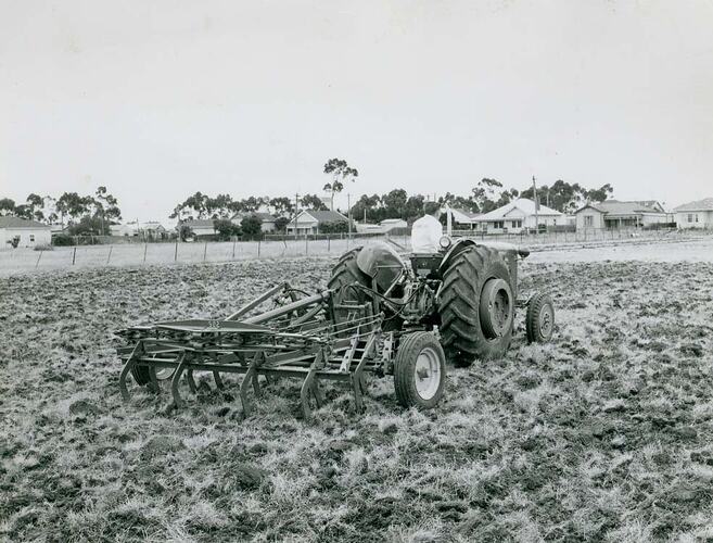 Rear view of a man driving a tractor coupled with a scarifier.