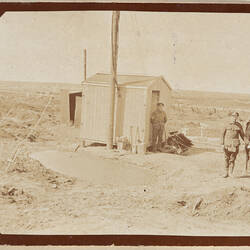 Two servicemen by small shed, one holding a horse by its bridle.