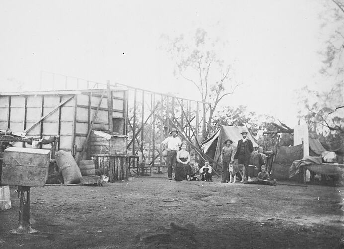 Family pose in front of their partially built new home. Tents are nearby.