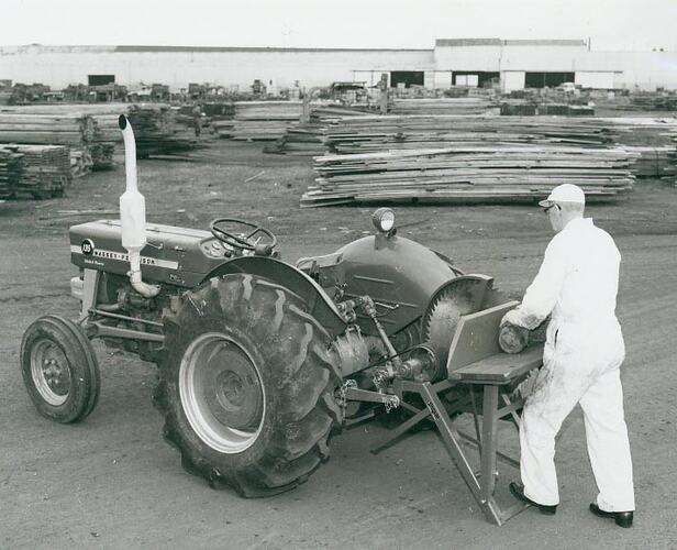 A man operating a saw bench coupled to a tractor.
