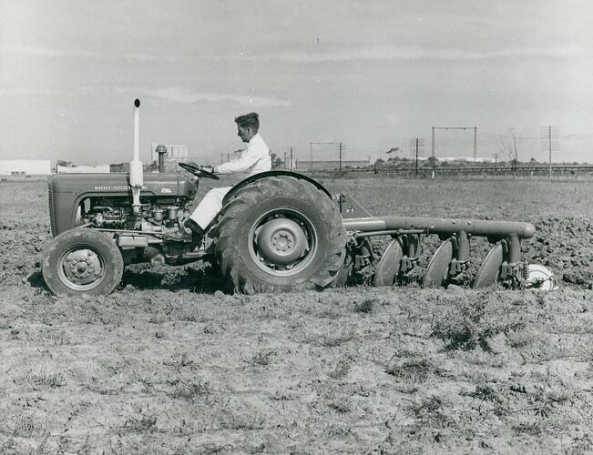 Side view of  a man driving a tractor with a disc plough attached in a field.