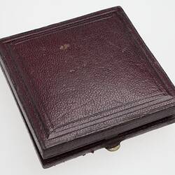 Closed square brown leather bound case with brass clasp at front.