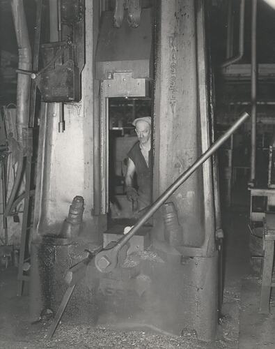 A man is operating a drop hammer forge.