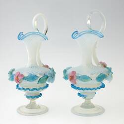 Pair of blue blown-glass ewer, spiral fluted neck, serpentine handle, flattened bulbous body layered with pink, blue, green flowers and leaves.