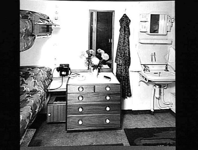 Ship interior. Bunk beds on left wall. Chest of drawers in centre, handbasin at right.
