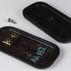 Rectangular dark photocell, open in half. Contains two spiral wires attached to inside wall via metal plate.