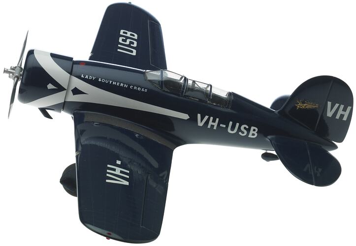 Metal dark blue model aeroplane with white stripe. Cockpit on top of body, silver propeller at front.