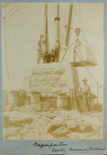 Four men posed on partially constructed stone monument, one man standing on ground to right.