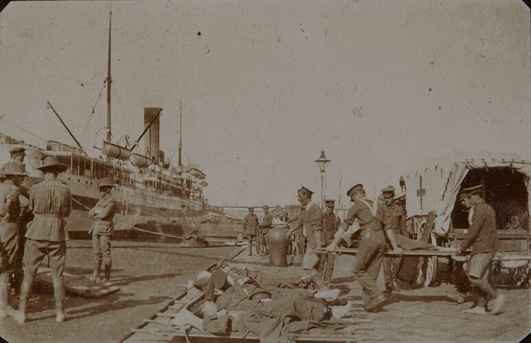 Loading wounded soldiers on stretchers laid on ground. Hospital Ship at left, Horsedrawn ambulance at right.