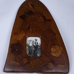 Wooden parquetry picture frame with curved top. Has black and white photograph of man with three women.
