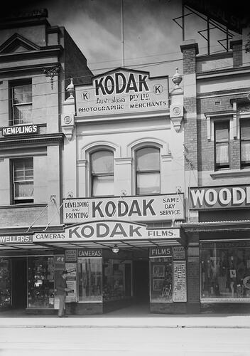 Shopfront with one storey. Has items front window display and three painted Kodak signs.
