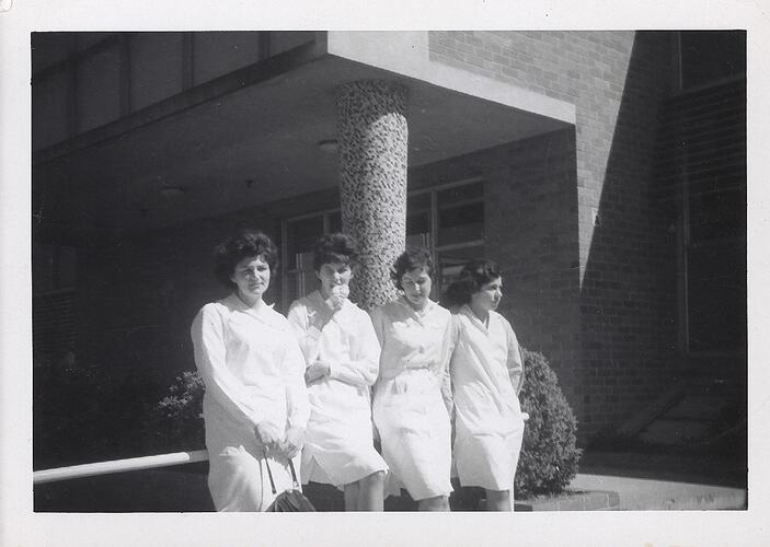Four women wearing factory uniforms, leaning against handrail .