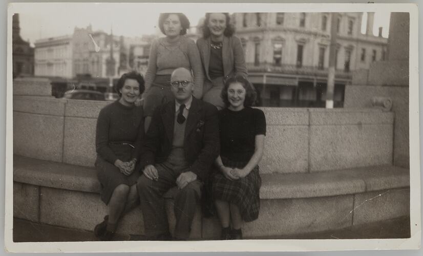 Four women and one man seated on curved seat.