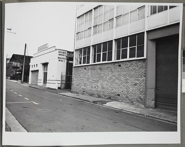 Street view of Bramil branded white building next to larger brick building.