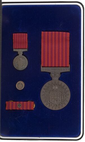 Two medals, one badge and one ribbon in blue fabric lined medal box.