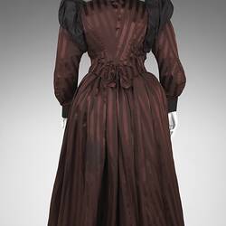 Back of burgundy and black satin striped dress. Fitted bodice, long sleeves, black billowed shoulders.