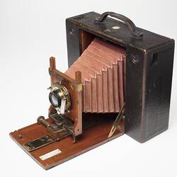 Brown leather-covered camera. Fold out wooden centre, red leather bellows. Front angle view.