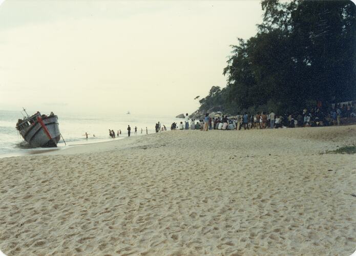 Large group of people on beach near boat.
