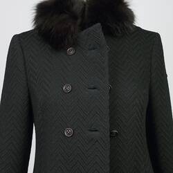 Black woollen double-breasted coat with fur collar and six plastic buttons. Bodice detail.