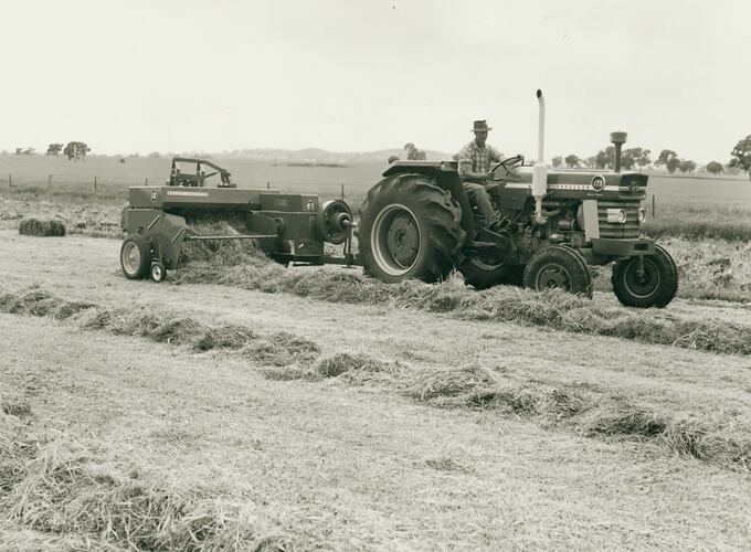 Man driving a tractor coupled to a pickup baler in a field of windrowed straw.