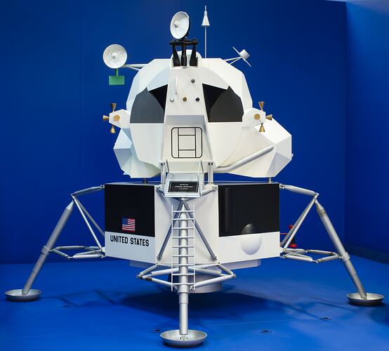 Four-legged lunar module with black and white body. Blue background.