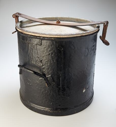 Black metal bucket with lid and one handle on side. Metal clip holds down lid.