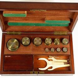 Standard gilt brass weights shown in an open wooden box.