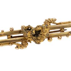 Gold double bar brooch with decorative detailing. Features small natural nugget in centre.
