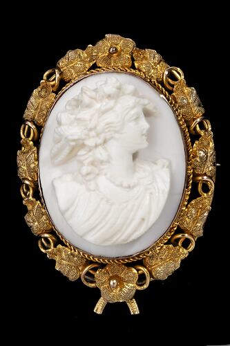 Oval brooch with gold framing white cameo relief woman facing right. Frame is gold leaves and tendrils.