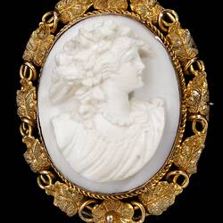 Oval brooch with gold framing white cameo relief woman facing right. Frame is gold leaves and tendrils.