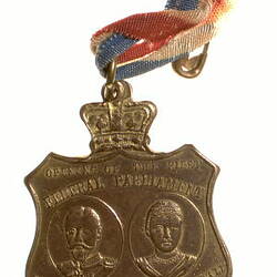 Shield-shaped medal with the Duke and Duchess of Cornwall & York faces. Crown on top. Red, yellow, blue ribbon