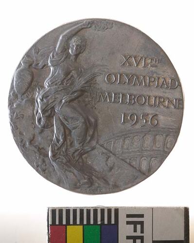Round medal with seated figure and text at right.