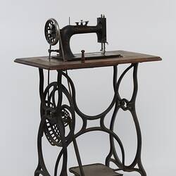 Sewing machine fitted to a metal frame with a wooden bench.