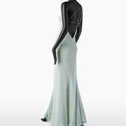 Back view of full length pale green silk evening slip dress. Sleeveless. Fastens at back with long green silk covered rope ties. Flared/fishtail skirt.