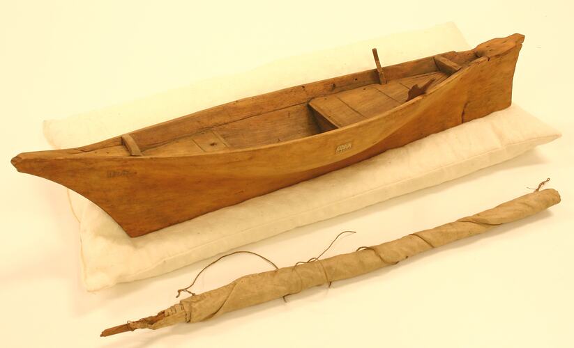 Model of a wooden sailing boat with sail and mast separate.