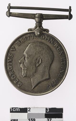 Round silver coloured medal with profile of man and text surrounding.