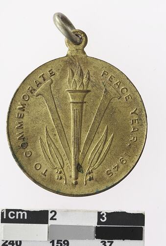 Gold coloured medal with image of flame on pillar, reading "TO COMMEMORATE PEACE YEAR 1945."